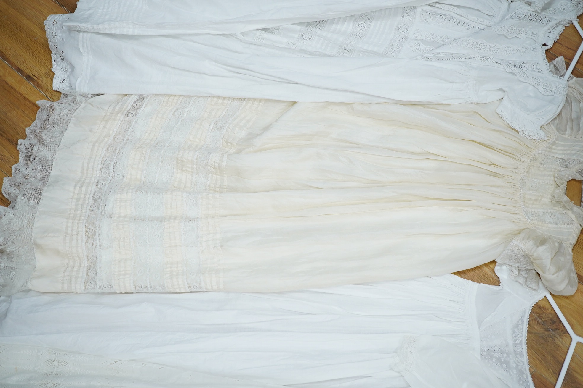 An Edwardian cream silk christening gown, together with four white christening gowns and a baby gown. The silk christening gown edged and inserted with lace and feather stitch embroidery, one Christening gown worked with